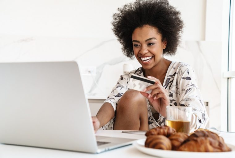 mulher morena fazendo compras online com seu cartão de crédito, com muita felicidade