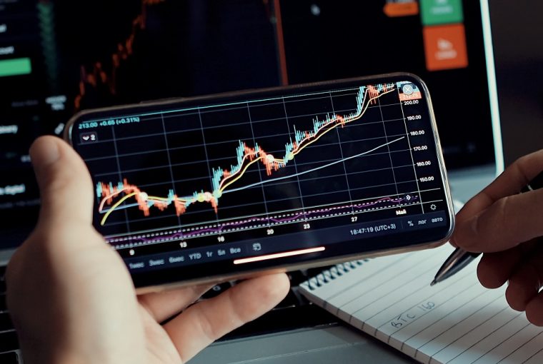 homem olhando mercado de ações no celular e fazendo anotações