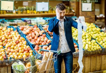 Homem com lista de compras no supermercado com aspecto assustado devido ao alto preço da cesta básica