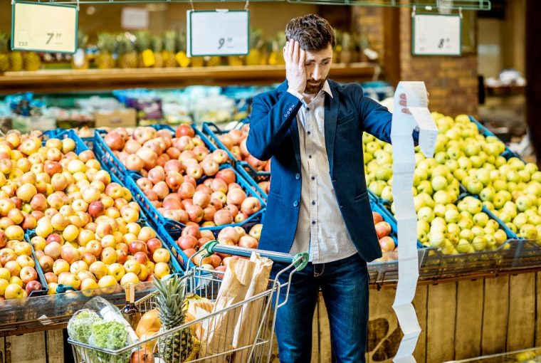 Homem com lista de compras no supermercado com aspecto assustado devido ao alto preço da cesta básica
