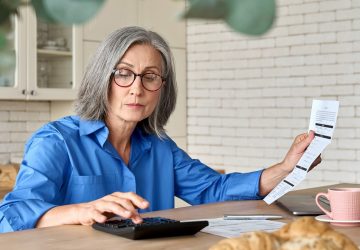 mulher idosa calculando as tarifas mostradas em um papel de banco digital ou tradicional