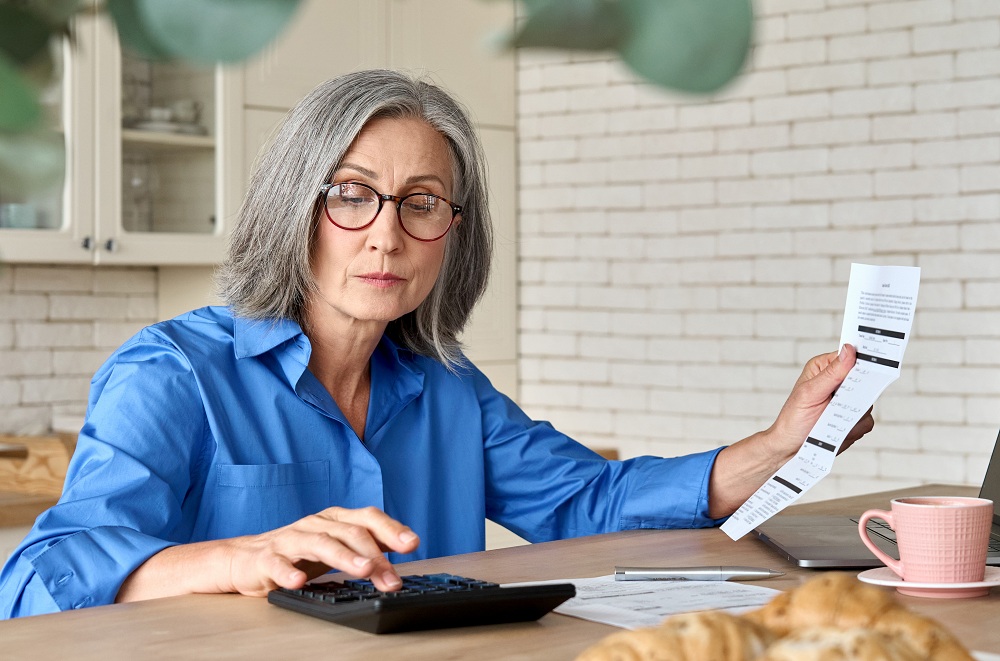 mulher idosa calculando as tarifas mostradas em um papel de banco digital ou tradicional