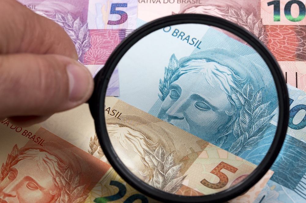 lupa sob notas de dinheiro real Brasil para simbolizar a nova lei do superendividamento no Brasil