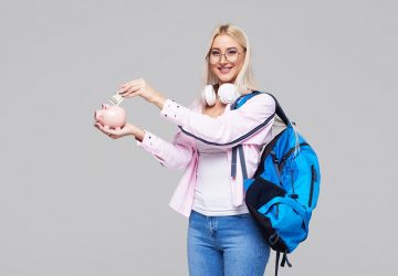 estudante mulher com mochila e fone de ouvido segurando um cofre em formato de porco e colocando dinheiro nele simbolizando dicas financeiras para universitários