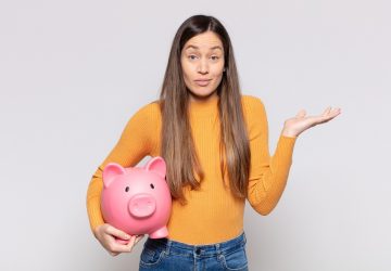 mulher segurando um cofre em formato de porco com semblante de dúvida sobre o que são juros compostos nos investimentos