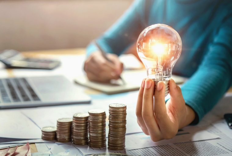 mão de mulher segurando lâmpada e fazendo cálculos, simbolizando um empréstimo na conta de luz como fazer