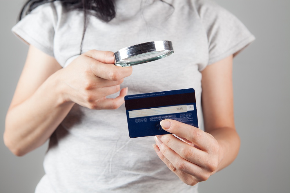 Mulher olhando para um cartão de banco com uma lupa para tentar descobrir os números do cartão de crédito