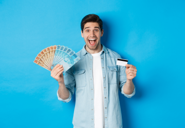 Homem atraente feliz parecendo espantado, mostrando dinheiro e cartão de crédito