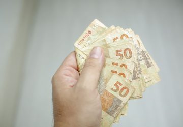 mão de homem segurando notas de cinquenta reais, simbolizando as Dicas para o salário render mais