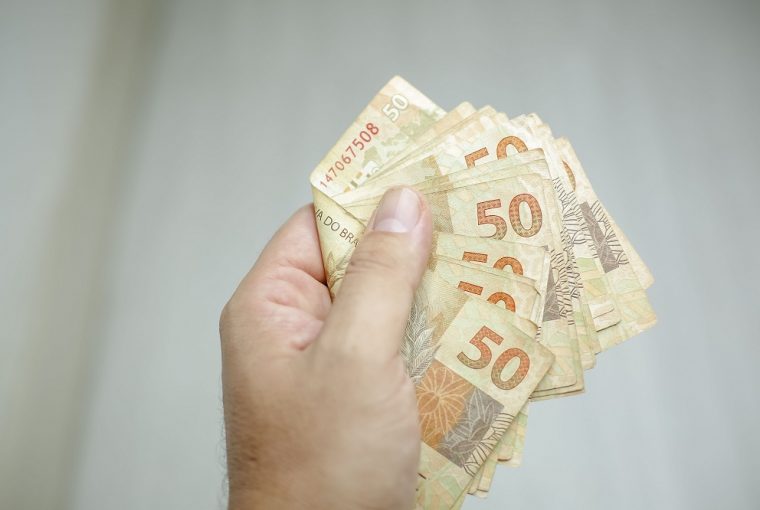 mão de homem segurando notas de cinquenta reais, simbolizando as Dicas para o salário render mais