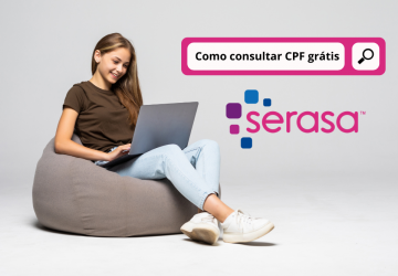 Mulher jovem feliz sentada no chão usando o laptop na parede cinza consultando o CPF grátis pelo Serasa