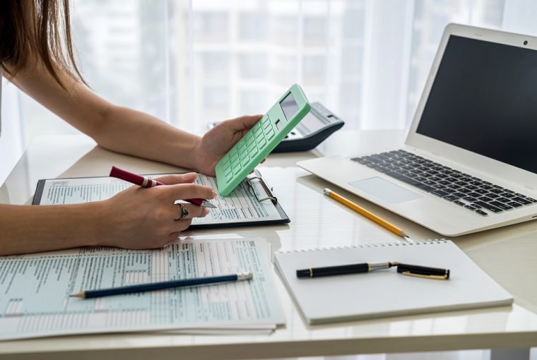 Mãos femininas com calculadora acima do formulário fiscal cair na malha fina