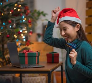 Mulher asiática feliz e animada com chapéu de papai noel usando cartão de crédito e laptop para fazer compras durante o feriado de natal em casa