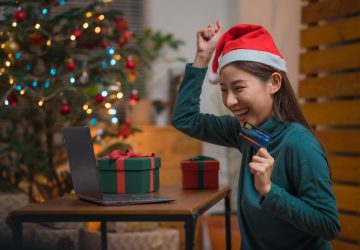 Mulher asiática feliz e animada com chapéu de papai noel usando cartão de crédito e laptop para fazer compras durante o feriado de natal em casa