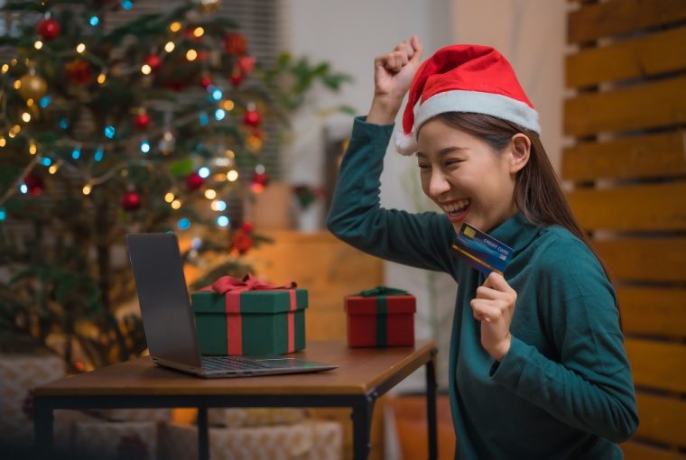 Mulher asiática feliz e animada com chapéu de papai noel usando cartão de crédito e laptop para fazer compras durante o feriado de natal em casa