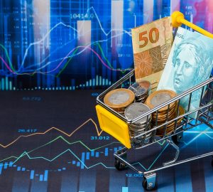 fundo de uma plataforma de Home Broker e um carrinho de compras com notas de cinquenta e cem reais e algumas moedas, simbolizando o passo a passo de como investir com pouco dinheiro