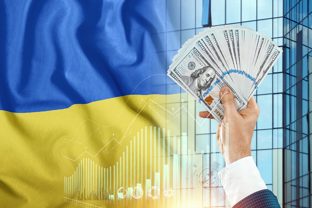 Dinheiro na mão de um homem no contexto da bandeira da ucrânia, simbolizando como o conflito e crise na Ucrânia e Rússia irá afetar a economia brasileira e mundial