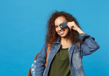 ovem estudante adolescente afro-americana em roupas jeans, mochila segurando cartão de crédito
