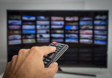 Mão pressionando controle remoto da tv SMART, para escolher entre TV por assinatura ou streaming para assistir