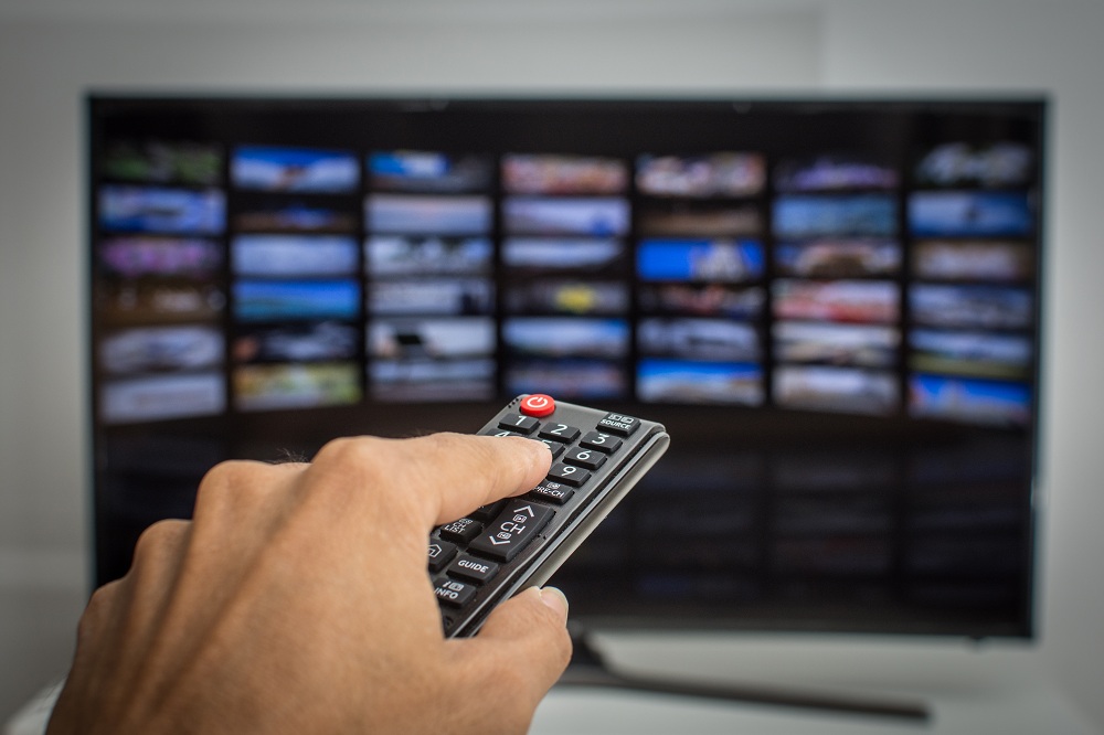 Mão pressionando controle remoto da tv SMART, para escolher entre TV por assinatura ou streaming para assistir