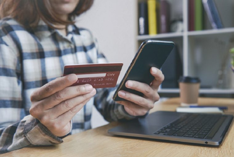 Jovem mulher segurando um cartão de crédito e usando telefone simulando como usar o seguro proteção de preço do cartão de crédito