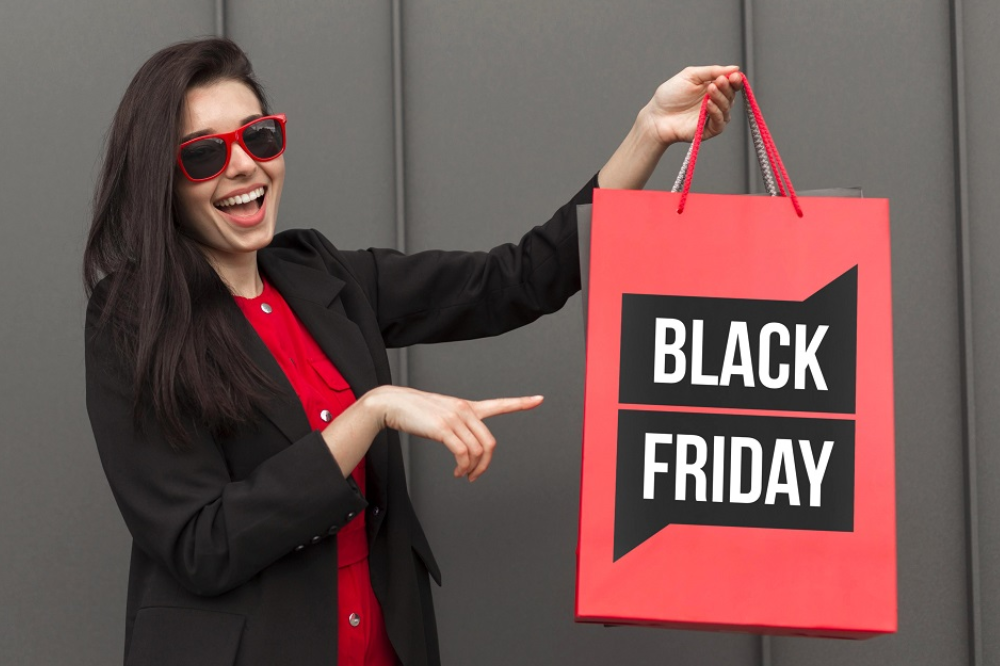 mulher de óculos vermelho apontando para sacola de compras escrito Black Friday, simbolizando como se preparar para a Black Friday
