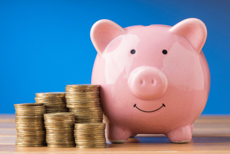 Cofre porquininho rosa ao lado de moedas em fundo azul, simbolizando o Dia da Poupança