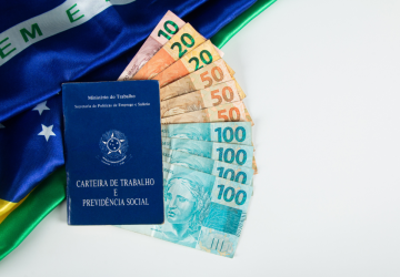 carteira de trabalho ao fundo bandeira do Brasil e notas de dinheiro simbolizando o pagamento do décimo terceiro salário