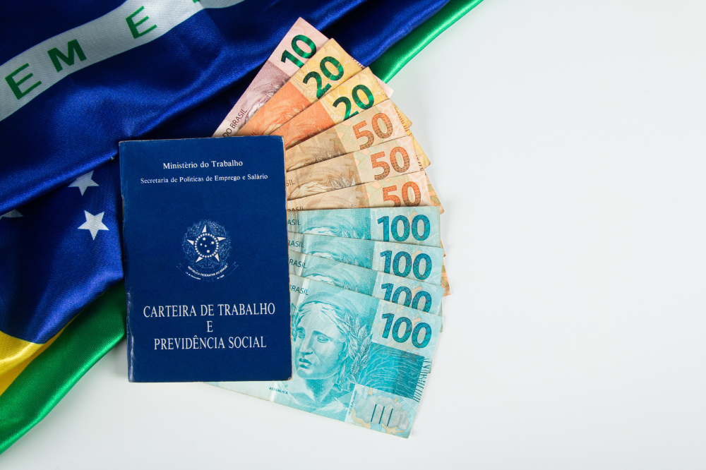 carteira de trabalho ao fundo bandeira do Brasil e notas de dinheiro simbolizando o pagamento do décimo terceiro salário